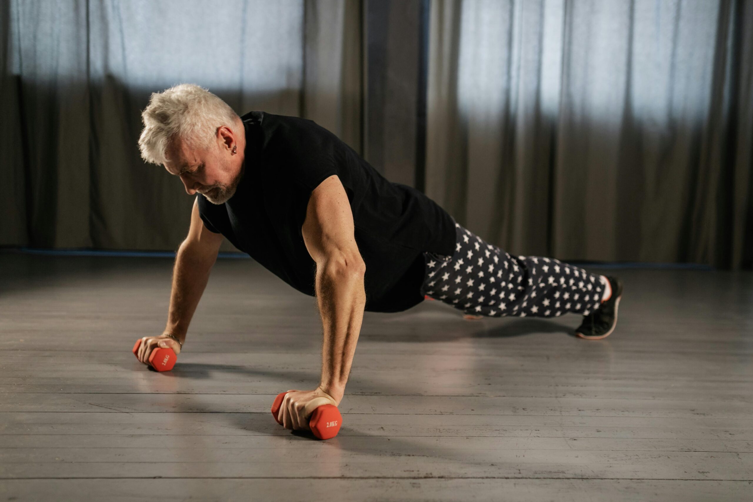 Senior man performing a push-up using dumbbells for strength training indoors.