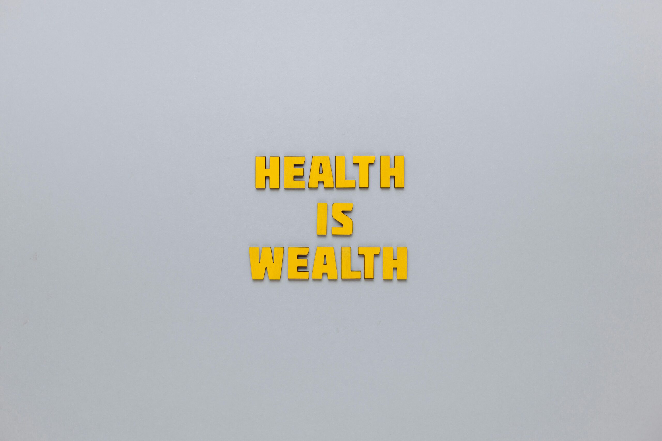 Inspirational phrase 'Health is Wealth' in bold yellow letters on a neutral gray background.