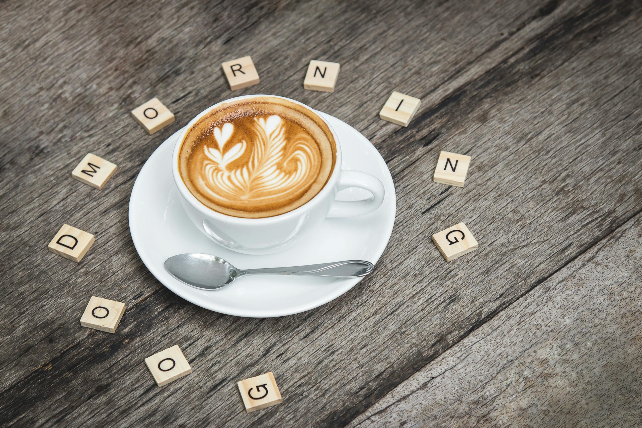 Cup of cappuccino with latte art surrounded by Scrabble letters spelling 'Good Morning'.